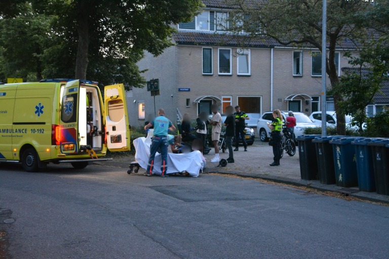 Ambulancepersoneel en politie bij een noodsituatie op straat met omstanders en een ambulance.