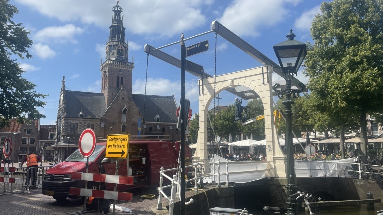 Bouwplaats bij een historische kerk met steiger en gele borden in de zon.