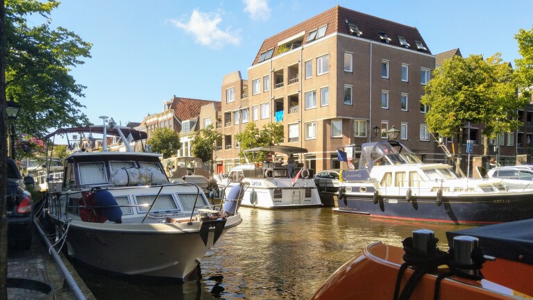 Boten aangemeerd langs de gracht met huizen op de achtergrond.