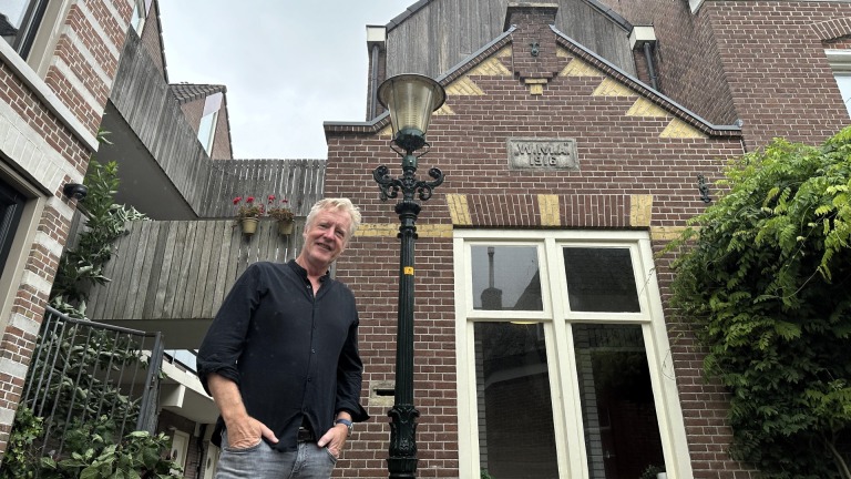 Man voor een oud huis van rode baksteen met bouwjaar 1916, naast een klassieke lantaarnpaal.