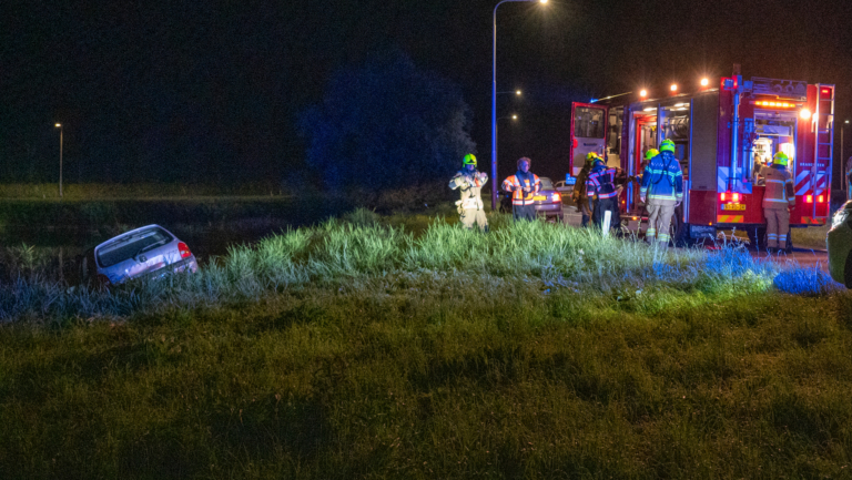 Brandweerlieden bij een auto-ongeluk langs een donkere weg, waarbij een auto in een greppel is beland.