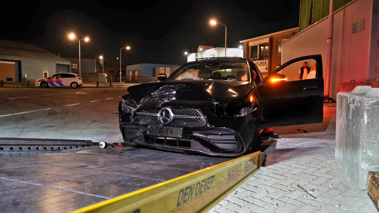 Zwarte auto met ernstige schade aan de voorkant wordt weggesleept, op de achtergrond staat een politieauto.