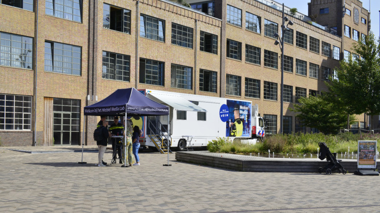 Een mobiel medialab van de politie met een tent op een plein voor een groot gebouw.