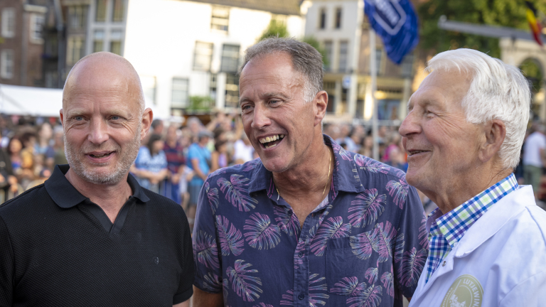 Drie lachende mensen op een drukke buitenlocatie.