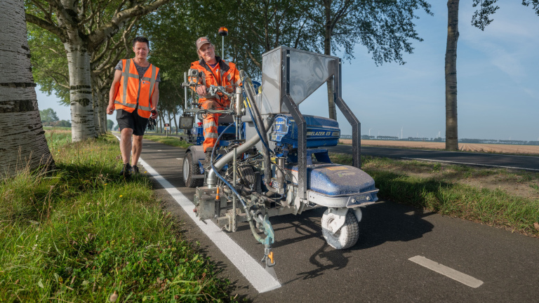 Twee wegwerkers met een lijnentrekker die een witte lijn op een fietspad aanbrengen.