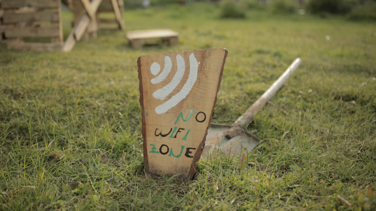 Houten bord met de handgeschilderde tekst "No WiFi Zone" op een grasveld.