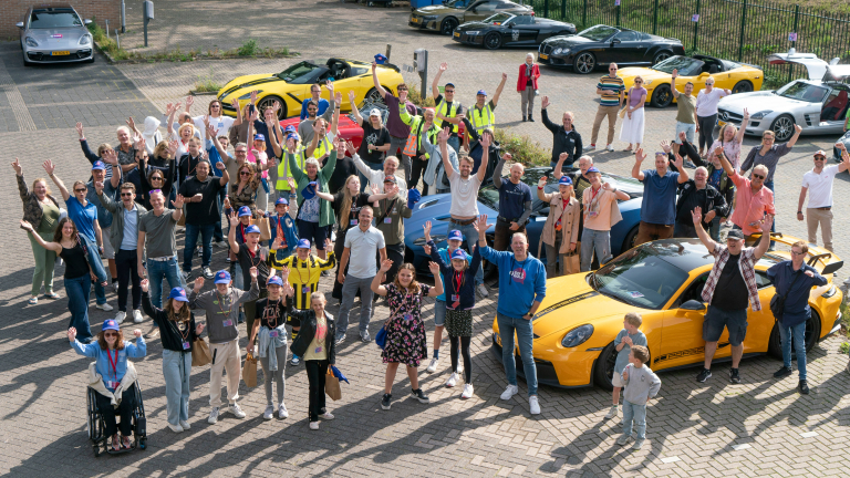 Groep mensen juicht en poseert bij luxe sportauto's op een parkeerplaats.