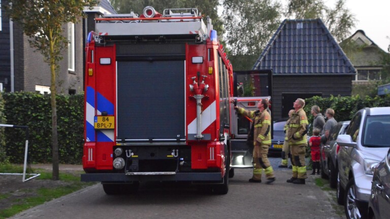 Brandweerauto met brandweerlieden en toeschouwers in een woonwijk.