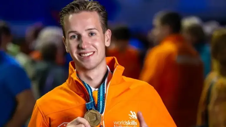 Man in oranje jack met "Wordskills" logo, die een medaille vasthoudt.