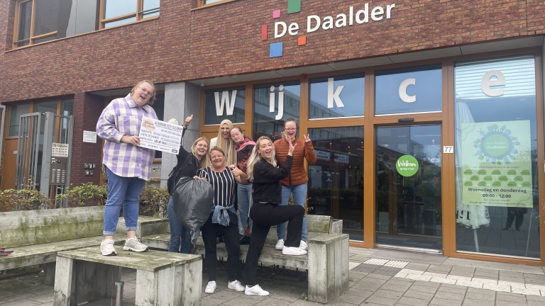 Een groep mensen poseert enthousiast met een certificaat en vuilniszakken voor buurthuis De Daalder in Alkmaar.