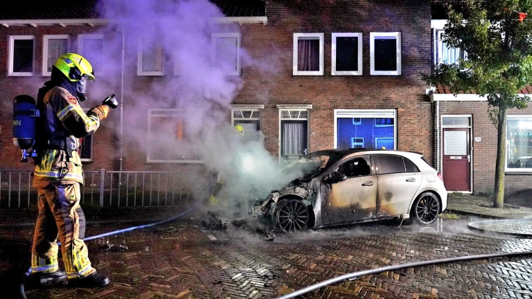 Brandweerman blust brandende auto op een straat in de nacht.