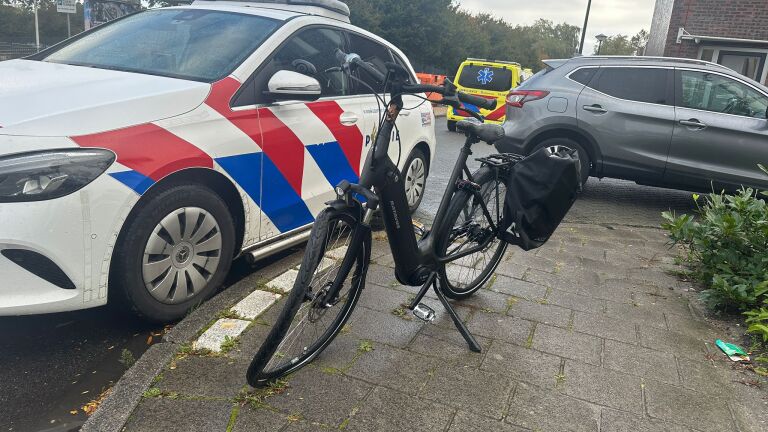 Politiewagen en fiets geparkeerd op stoep met ambulance op de achtergrond.