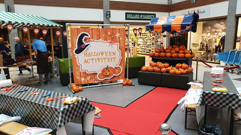 Halloween-activiteit in winkelcentrum met pompoenen en versierde kraampjes.