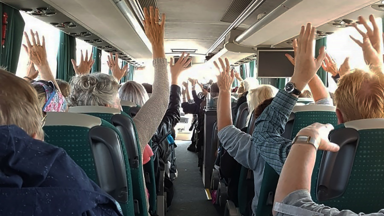 Mensen in een bus steken hun handen in de lucht.