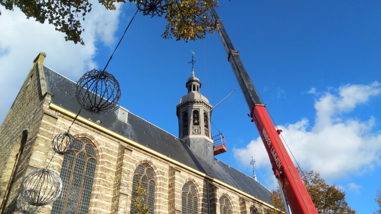 Een kraan naast een kerk met klokkentoren, met decoratieve lichtstructuren aan draden gespannen.