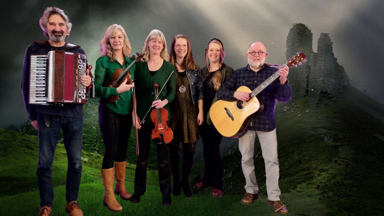 Een groep van zes personen met muziekinstrumenten poseert voor een achtergrond van een groen landschap met ruïnes.