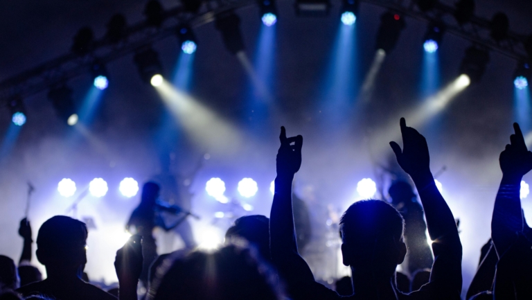 Publiek bij een concert met felle blauwe en witte podiumlichten.