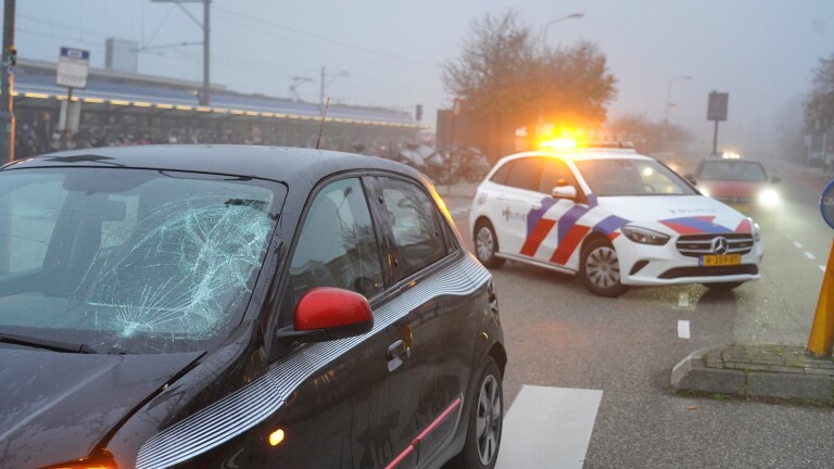 Auto met kapotte voorruit en politieauto met zwaailicht op straat.