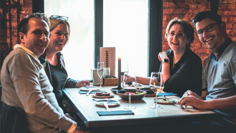 Vier mensen lachen en zitten aan een gedekte tafel in een restaurant.