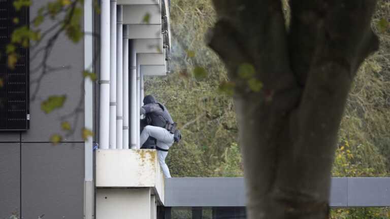 Persoon in donkere kleding en rugzak klimt langs de zijkant van een gebouw.