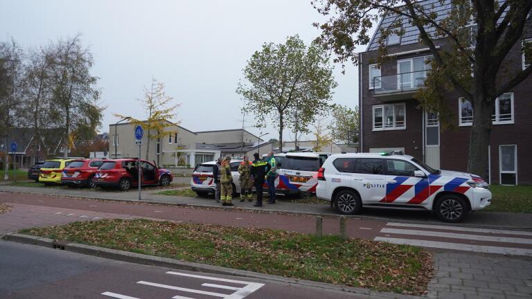 Politie- en brandweerauto's geparkeerd langs een straat met enkele agenten en brandweerlieden die bij elkaar staan.