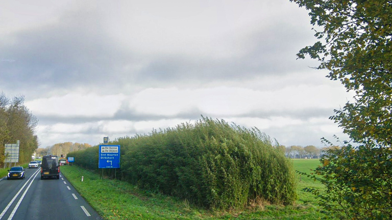 Weg met auto's en een verkeersbord naar Sint Maarten en Dirkshorn, omgeven door groen en bewolkte lucht.