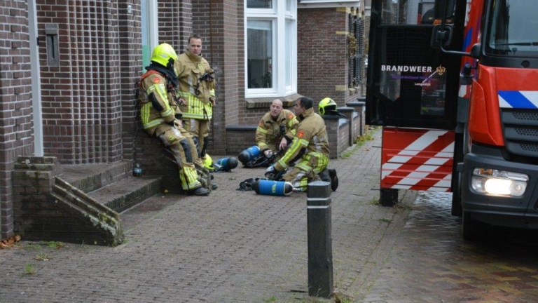 Brandweerlieden in uniform ontspannen naast een brandweerauto op een stoep.