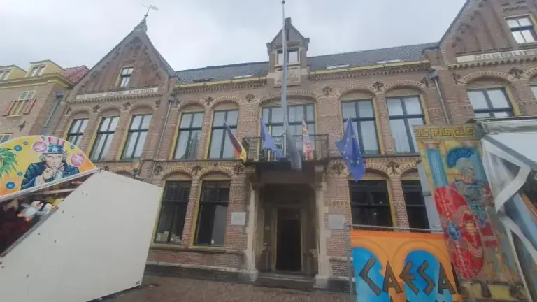 Bakstenen gebouw met verschillende vlaggen en kleurrijke graffiti-panelen aan de zijkant.