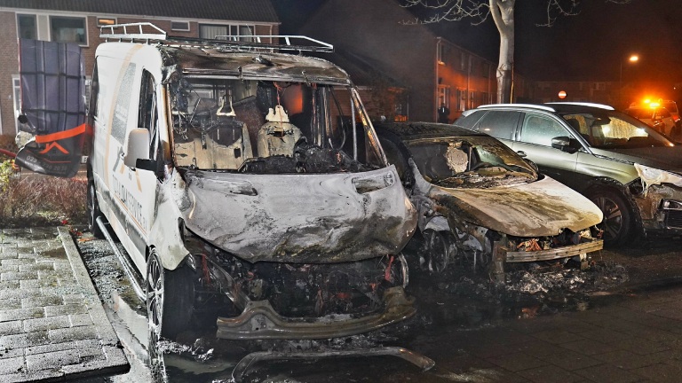 Twee auto's zijn in de nacht beschadigd door brand, geparkeerd langs een stoep.