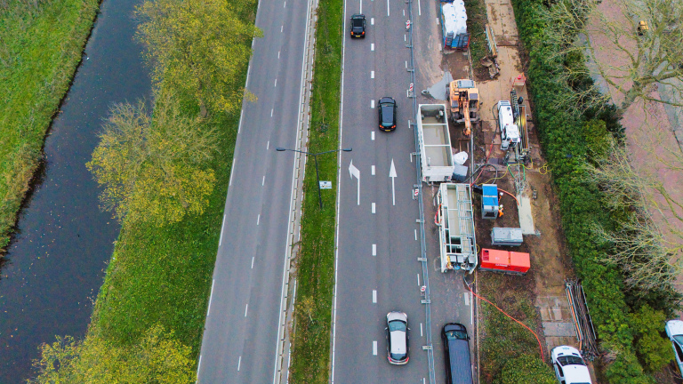 Luchtfoto van een weg langs een kanaal met auto's en een bouwplaats aan de rechterkant.