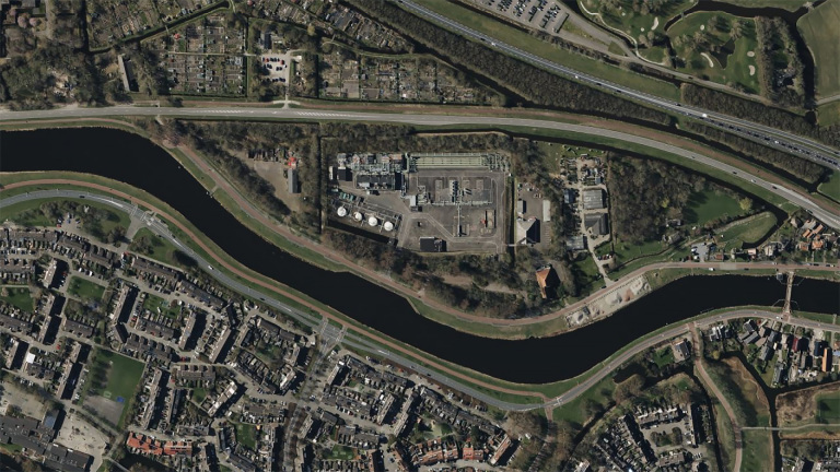 Luchtfoto van een stedelijk gebied met gebogen waterweg, infrastructuur en gebouwen, omringd door groen.