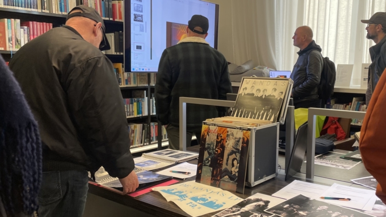 Mensen staan rondom een tafel met boeken en fotomateriaal in een bibliotheek.