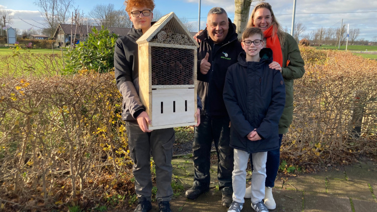 Vier mensen poseren buiten met een groot insectenhotel.