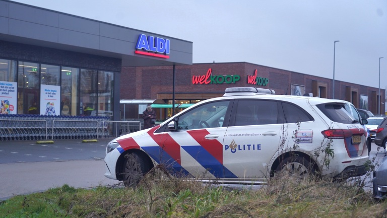 Politieauto geparkeerd voor een Aldi-supermarkt en Welkoop-winkel.