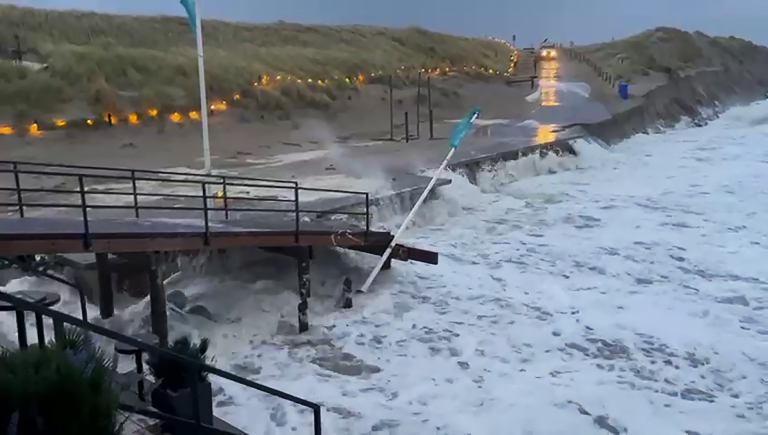 Stormachtige zee overspoelt een houten loopbrug aan de kustlijn.