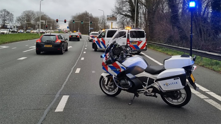 Politiemotor en -voertuigen op de snelweg met blauwe zwaailichten aan, verkeer wordt geblokkeerd.