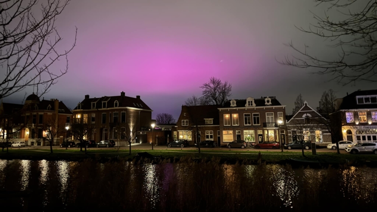 Rij huizen langs een kanaal met een paars verlichte lucht erboven.