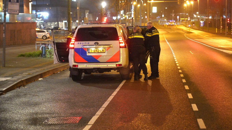 Drie politieagenten staan bij een politieauto op een verlaten straat 's nachts.