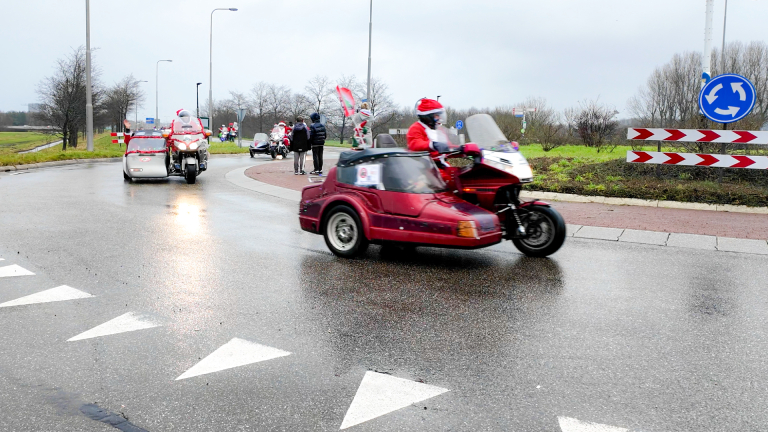 Motorrijders met kerstversierde zijspan outfits rijden op een rotonde op een regenachtige dag.