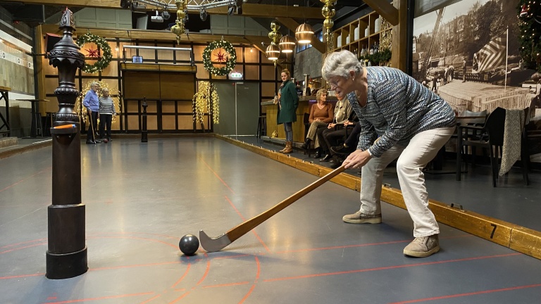 Een persoon speelt krulbollen in een indoor locatie met feestelijke decoraties.