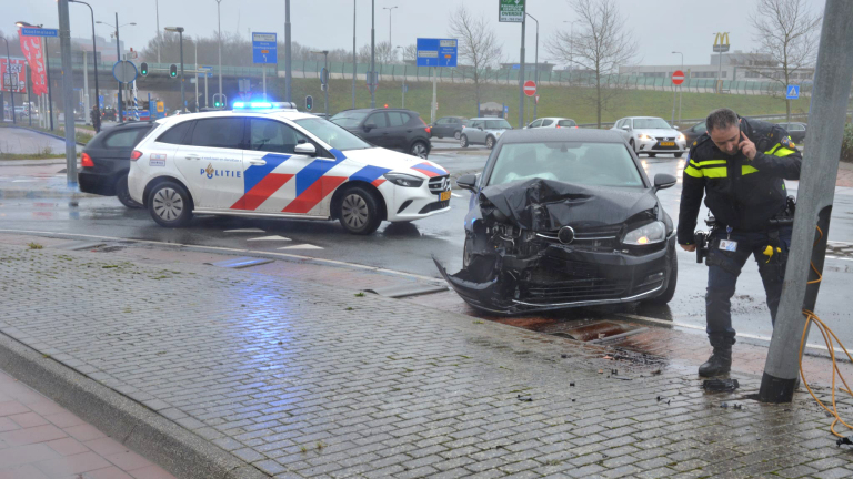 Een beschadigde zwarte auto na een aanrijding, met een politieauto en een agent ter plaatse.