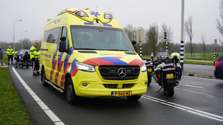 Gele ambulance op de weg, met politieagenten en een motorfiets op de achtergrond.