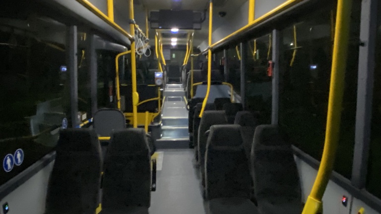 Interieur van een lege bus met zwarte stoelen en gele handgrepen.