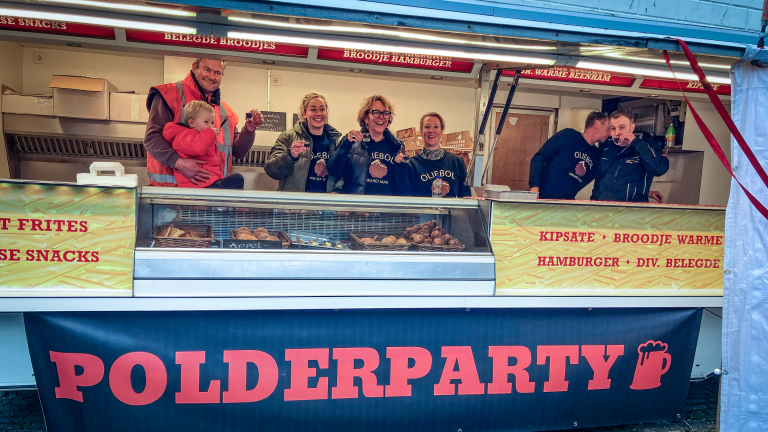 Personen staan achter een foodtruck met de tekst "POLDERPARTY", er zijn snacks zoals frietjes en oliebollen te zien.