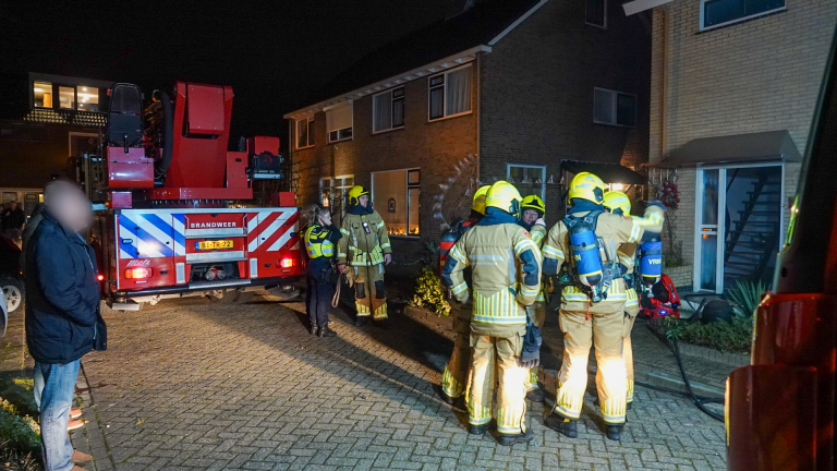 Brandweerlieden en een politieagent bij een brandweerwagen voor een huis in de avond.