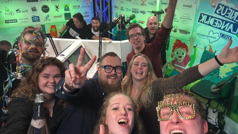 Een groep vrolijke mensen maakt een selfie in een kleurrijke studio met decoratieve elementen en flessen drank.