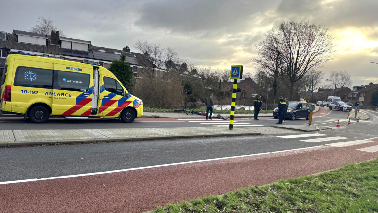 Een ambulance en politieauto's bij een zebrapad; mensen staan eromheen en een fiets ligt op de grond.