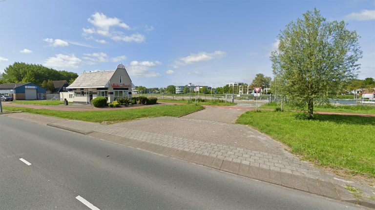 Een gebouw met de naam "Italiaans" aan de straatkant, omgeven door groen en een boom, onder een blauwe hemel met enkele wolken.