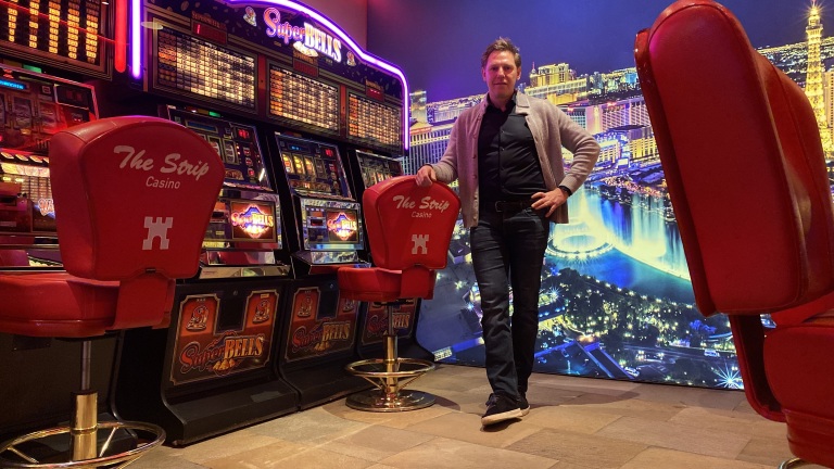 Man poseert in een casino bij gokautomaten met een fotomuur van Las Vegas op de achtergrond.