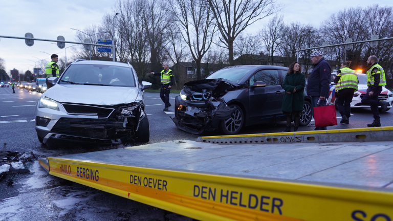 Twee auto's met schade na botsing op een kruispunt, omringd door politieagenten en omstanders.